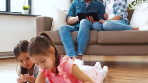 Family relaxes at home, children drawing, parents use tablet