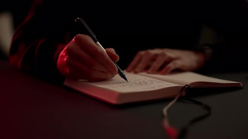 Man Writing in a Notebook in Low Lighting