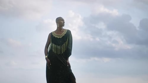 LGBTQIA Black Person in Boutique Dress Jewelry Stands on Rock on Stunning Ocean Coastline Skyline