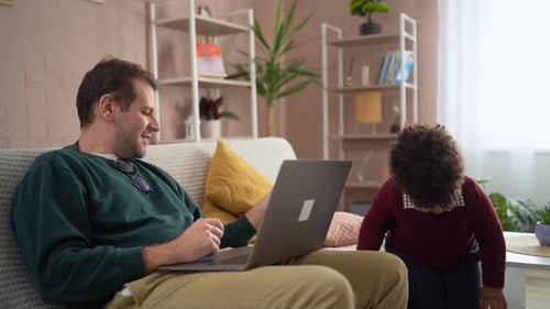 Man Works on Laptop While Child Plays Nearby