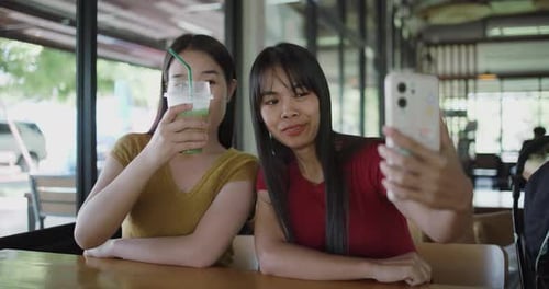 Two siblings happily chat with friends via smartphones in a coffee shop.
