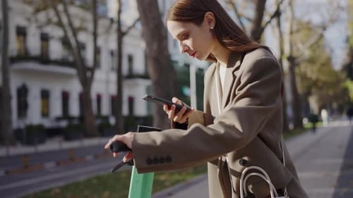 Young Professional Woman Using Smartphone While on Electric Scooter in City