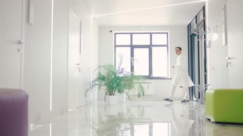 Male Doctor in Eyeglasses Hurrying Through a Modern Hospital Corridor to Urgent Surgery