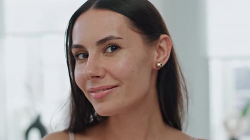 Smiling woman putting on earrings in her house