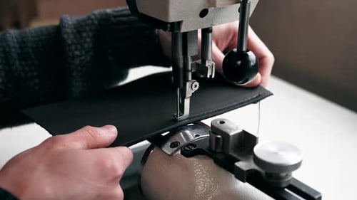Close-up of the tailor's hands. Close-up sewing machine. The tailor sews a purse made leather