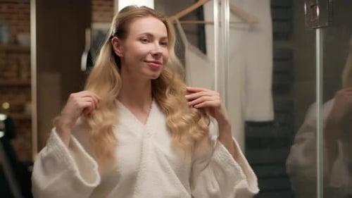 Woman with Blonde Hair Styling in Bathroom Mirror