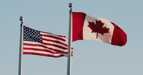 American and Canadian Flags Waving Against Blue Sky
