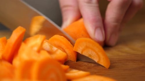 Hand Slicing Fresh Carrot on Wooden Board