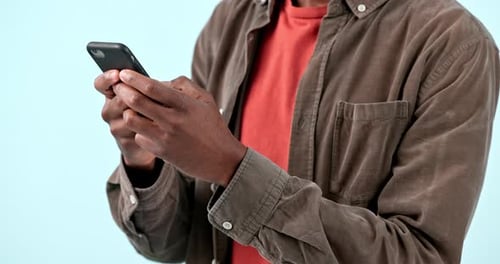 Hands, smartphone and man typing in studio isolated on blue background