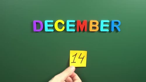 Hand sticking a sticker 14 December calendar day on school board. 14 date of December. Fourteenth