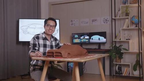 Asian Man Automotive Designer Smiling To The Camera While Working On The Sculpture Of Car Clay