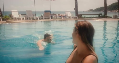 Happy couple enjoying vacations having fun in swimming pool at resort in midday