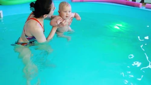 Female coach deeps the small kid into the water in the swimming pool.