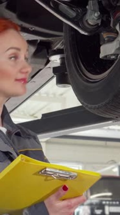 Skilled Female Mechanic Inspecting Car Wheels While Jotting Down Notes