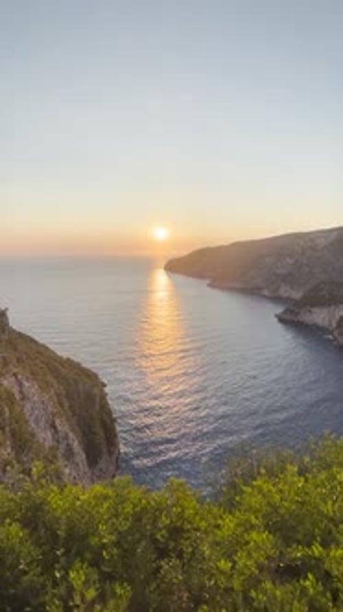 A beautiful view of the sunset from a cliff next to the water as the hill slop decreases towards the