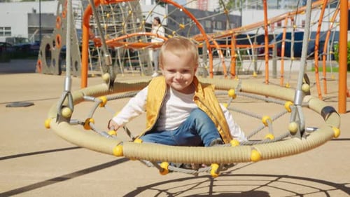 Slow motion of cheerful baby boy having fun and joy while swinging on the playground