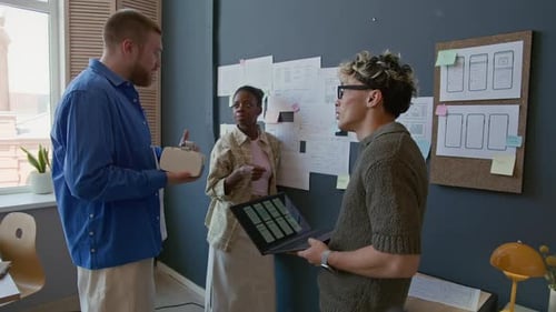 Diverse Team Of UX Designers Discussing Mobile App Standing by Wall at Office