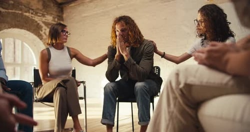 A Man with Curly Red Hair in a Green Gray Sweater Leans on His Elbows and Brings His Palms to His