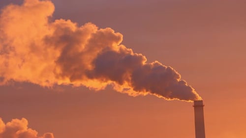 At Sunset a Factory Chimney Expels Dense Smoke Contrasting the Vivid Sky and Industrial Scene