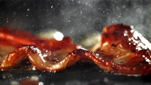 Close up of sizzling bacon cooking on stovetop