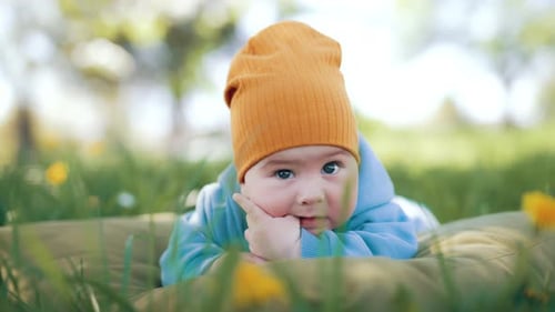 Kaukasischer Junge, der sich im grünen Gras ausruht. Das kleine Kind liegt auf dem Bauch und kaut sich am Daumen
.
