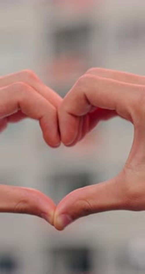 Fingers Forming Heart Shape Against a Building