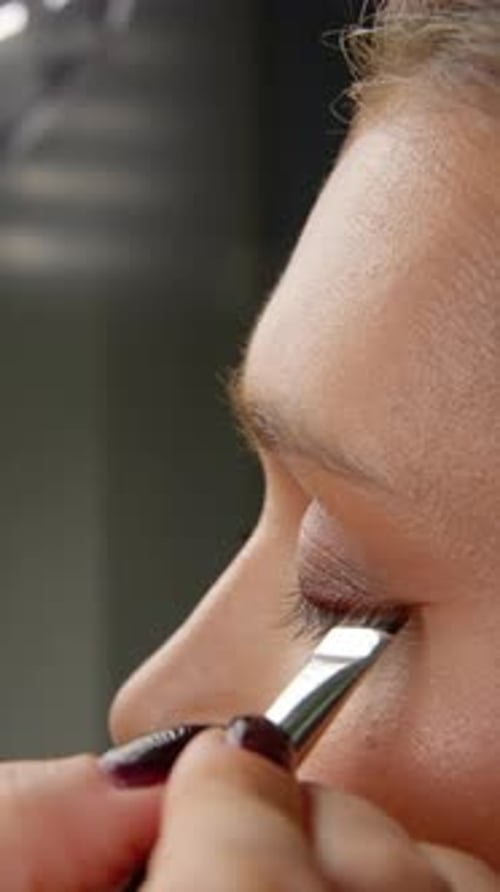 Skilled Makeup Artist Applying Shimmery Eyeshadow on Upper Eyelid of Young Caucasian Model