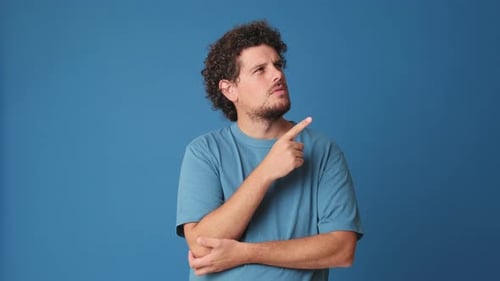 Young man making choice, having an idea, isolated on blue background in studio