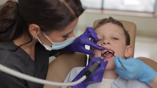 Kid in dental office. Dentist doing hygienic teeth cleaning to a boy sitting in a chair