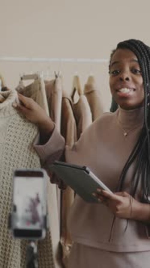 Vertical of Black Woman Demonstrating Clothes while Vlogging in Store