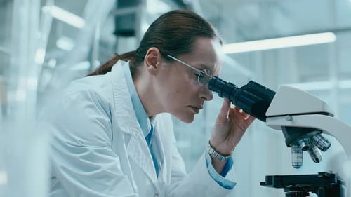 Woman Scientist Looking Through Microscope in Laboratory