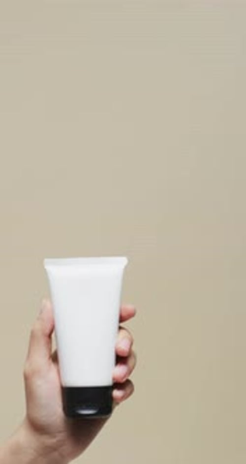 Hand Holds White Tube of Lotion or Cream