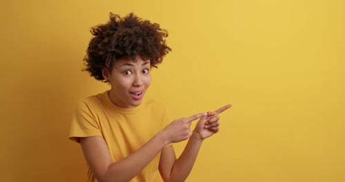 Enthusiastic woman points and smiles on yellow background