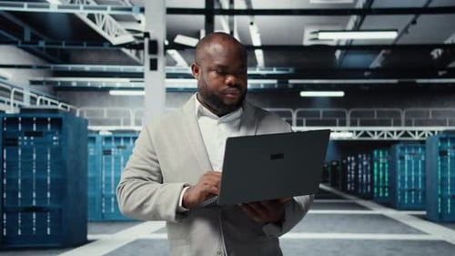 Technician Walking in Data Center Using Laptop to Check Hardware