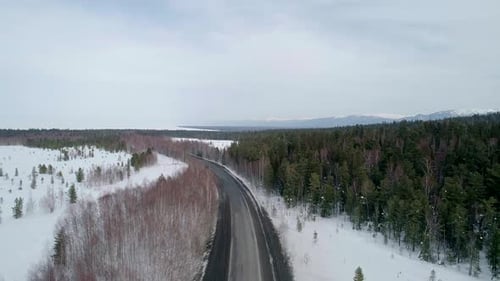 Aerial View Intercity Road Surrounded with Evergreen Trees on the Snow and Mountains with Snowcapped
