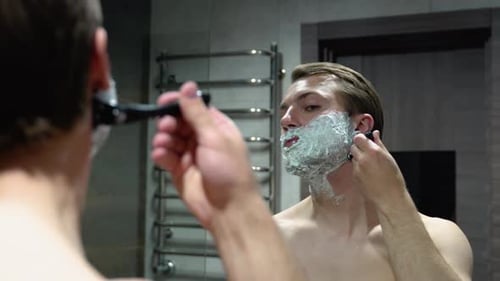Young Man Shaves His Face in Bathroom