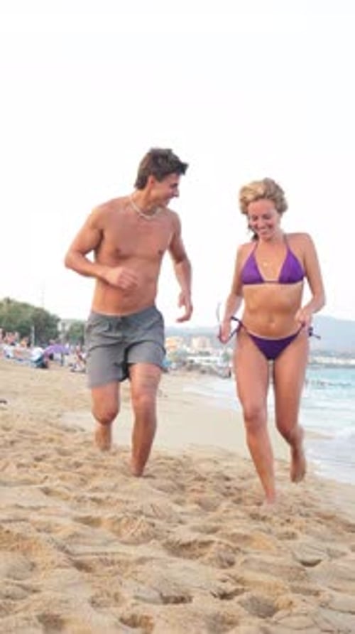 Joyful Young Couple Running Along the Sandy Beach During a Sunny Summer Day Filled with Laughter
