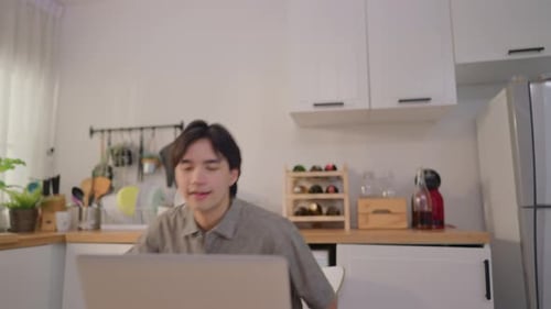 Smiling Man Using Laptop and Drinking Coffee in Kitchen