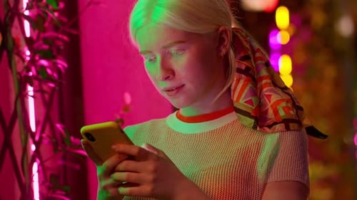 Cute Pretty Albino Teen Girl Using Mobile Phone on Neon Street