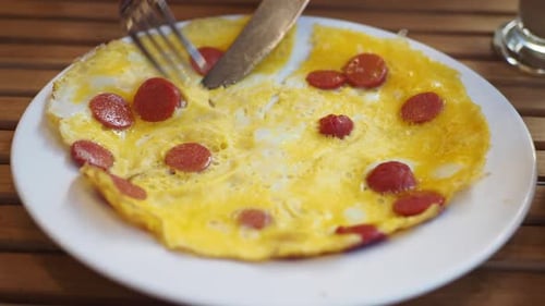 Cutting Omelet with Sausage on White Plate