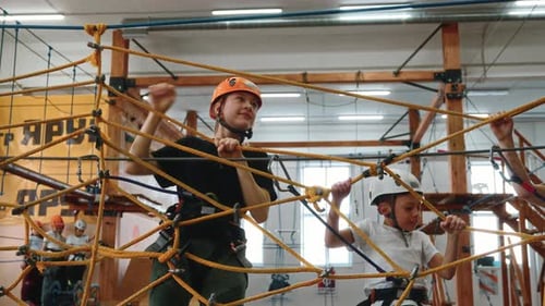 A Boy and a Girl Go Through an Obstacle Course in a Rope Park Indoors