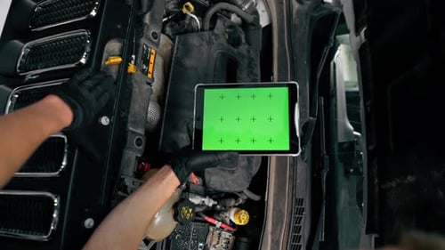 Close-up of a hand with a tablet on which the green screen is open against the background of a car