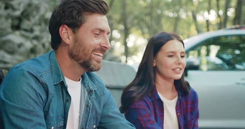 Portrait of happy caucasian family roasts sausages on campfire in tourist camp in forest. Man woman