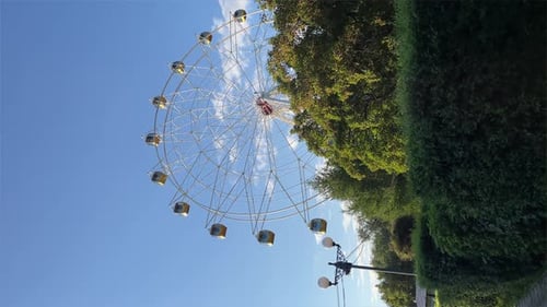 A Colorful Ferris Wheel Spinning Slowly in an Amusement Park at Sunny Summer Day Entertainment and