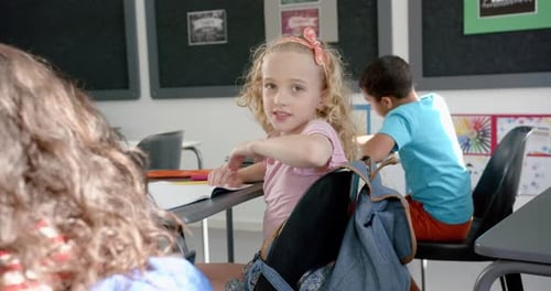 Caucasian girl with blonde curly hair smiles in a classroom setting in school