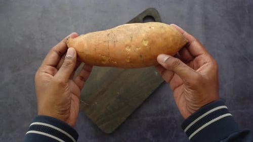 Hands holding a raw sweet potato over cutting board