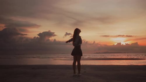 Young Woman Standing Raising Her Hands and Looking at Beautiful Incredible Sunset at Ocean Inspired