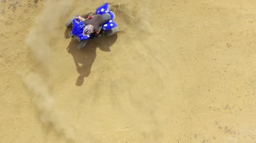 A man riding a quad bike on a sandy area of a farm