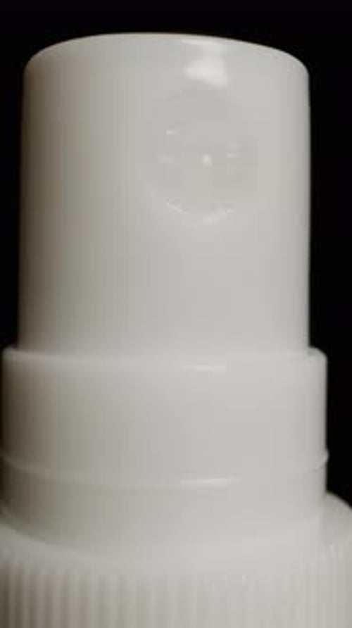Vertical video. White spray bottle with a push spray nozzle. Close-up on a black background.