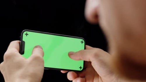 A Man Playing a Smartphone Game Holding It Horizontally. Green Screen Mockup on the Smartphone.